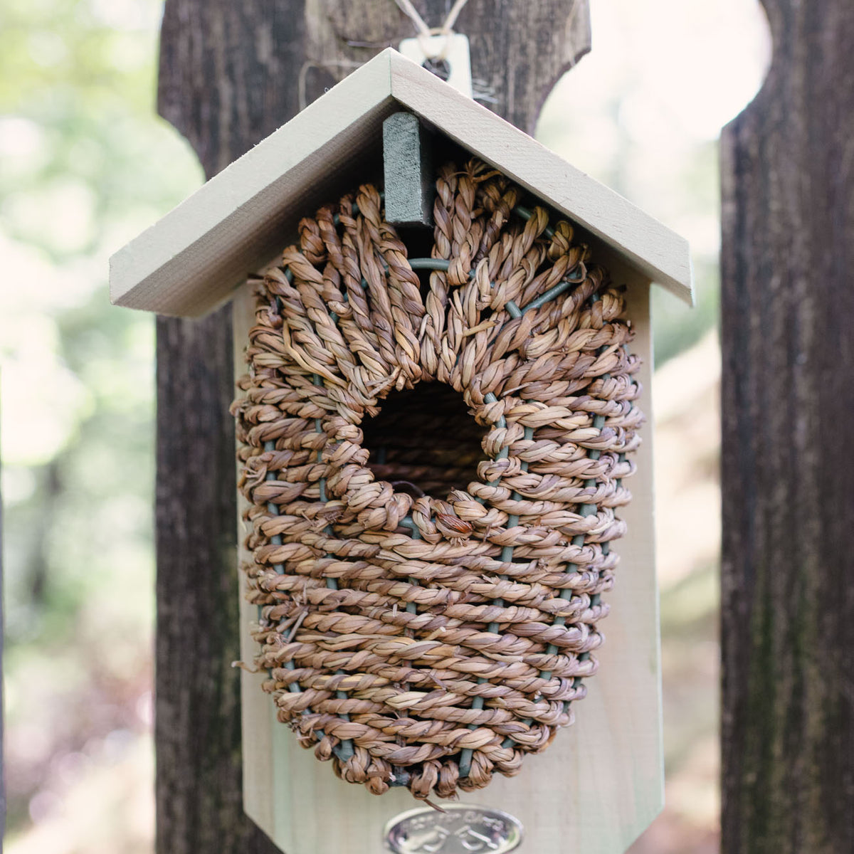 Whitewashed wooden birdhouse with tightly woven natural seagrass nesting pocket, mounted on weathered post