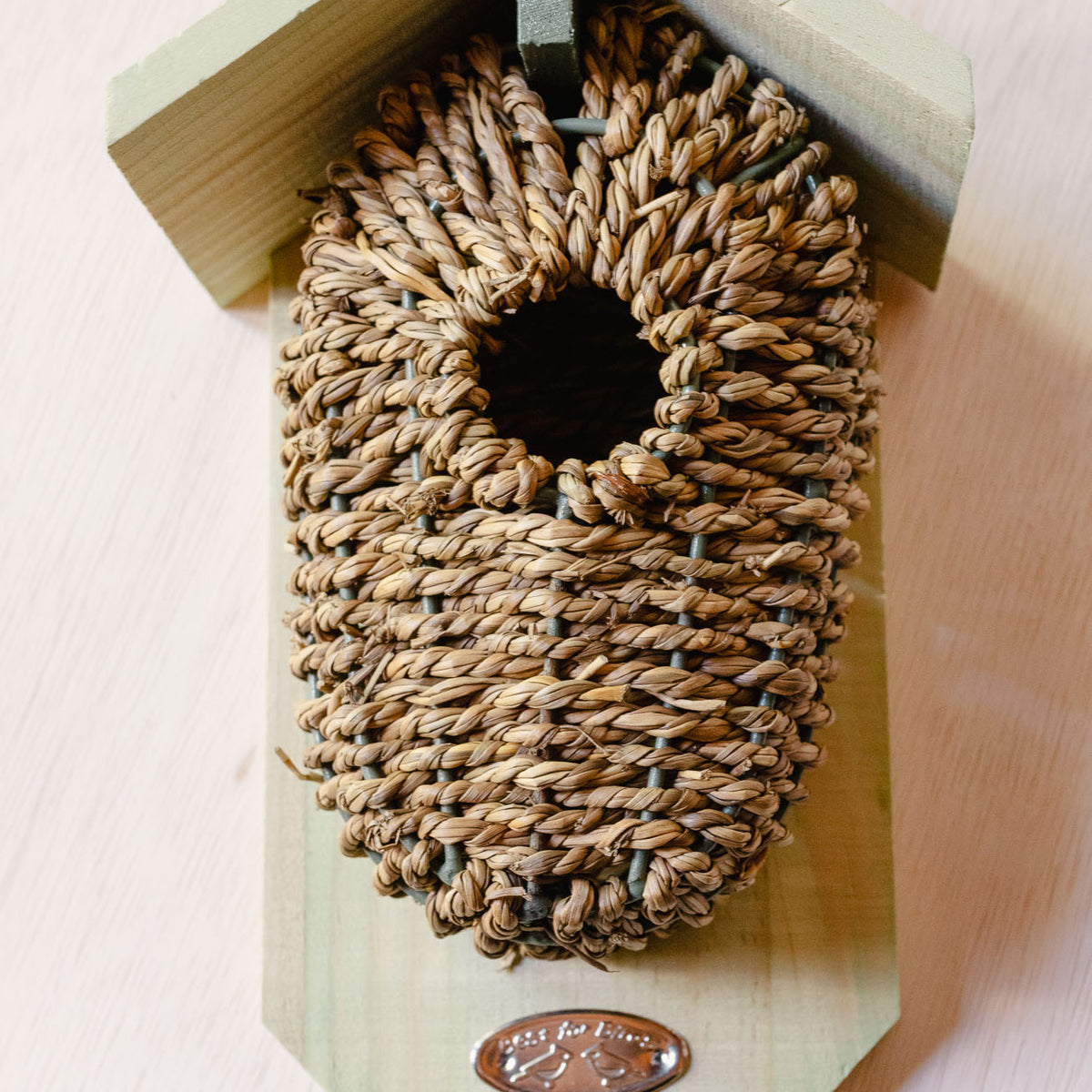 Whitewashed wood birdhouse with tan woven seagrass nesting pocket covering the entrance, mounted bracket visible