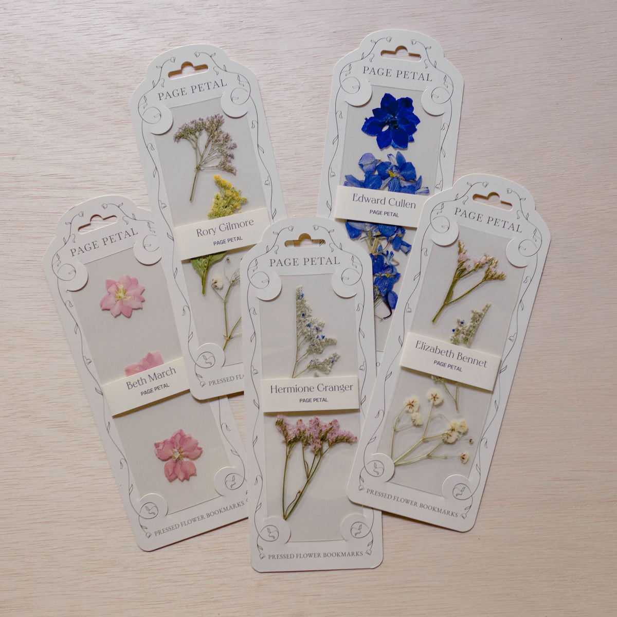 Five Page Petal floral bookmarks with pressed flowers—pink blossoms, blue petals, yellow botanical, delicate green herbs, and brown foliage—on cream cardstock with decorated headers.