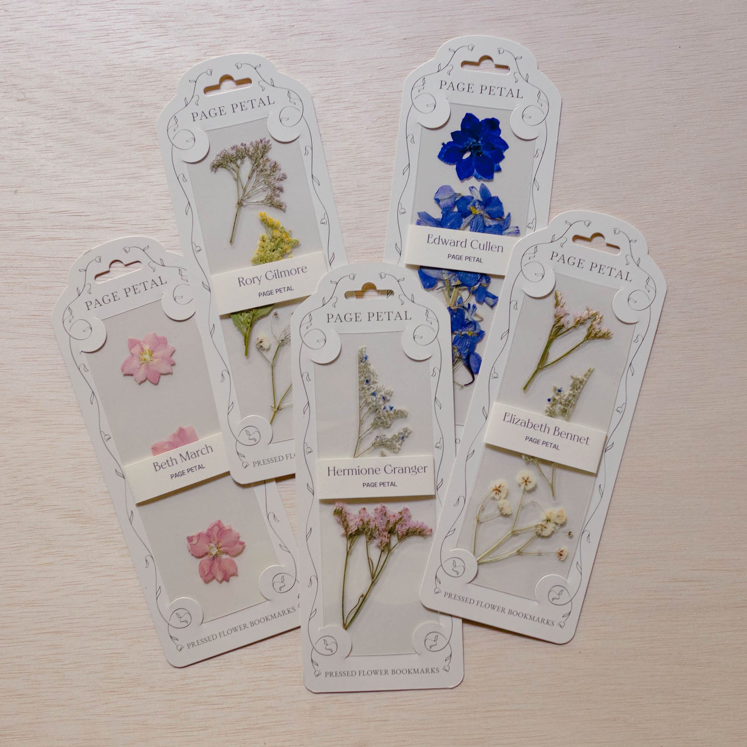 Five Page Petal floral bookmarks with pressed flowers—pink blossoms, blue petals, yellow botanical, delicate green herbs, and brown foliage—on cream cardstock with decorated headers.