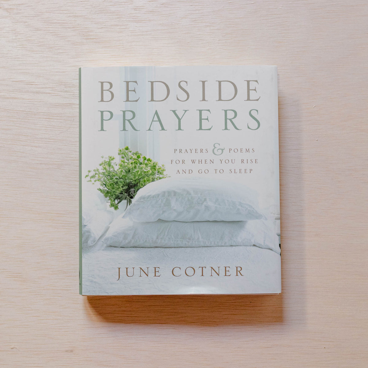 Bedside Prayers hardcover book by June Cotner on wooden surface, cover featuring green foliage in white vase and pale blue pillows