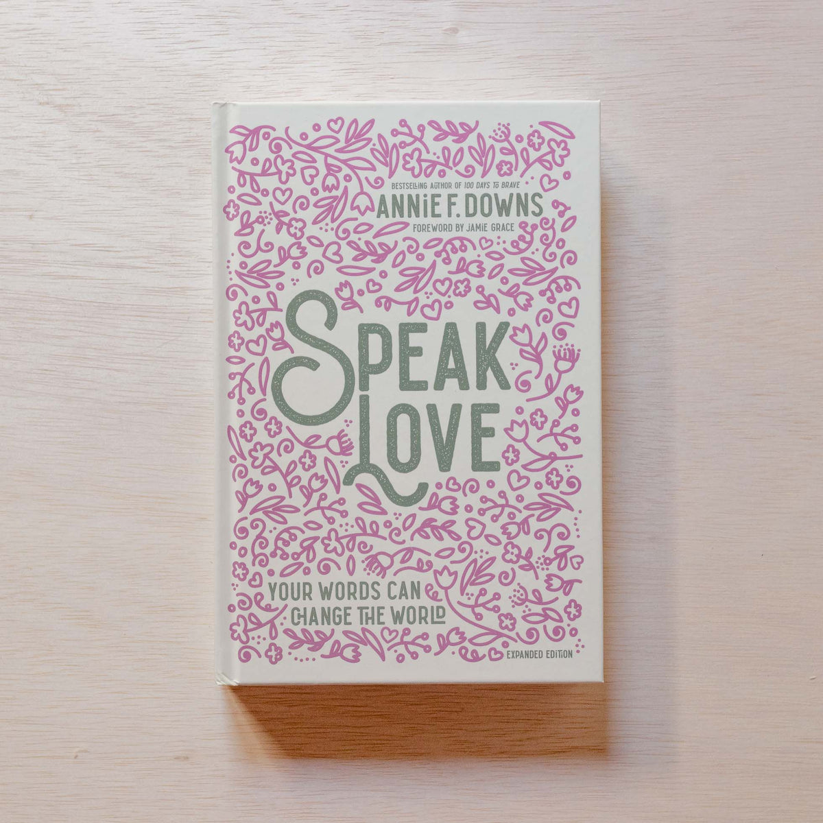"Speak Love" paperback by Annie F. Downs with pink floral patterned cover and gray title text on light wood background