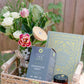 Wicker basket with flowers, candles, and books on a blurred outdoor background