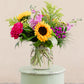 Colorful bouquet of flowers in a clear vase on a light green pedestal against a beige background