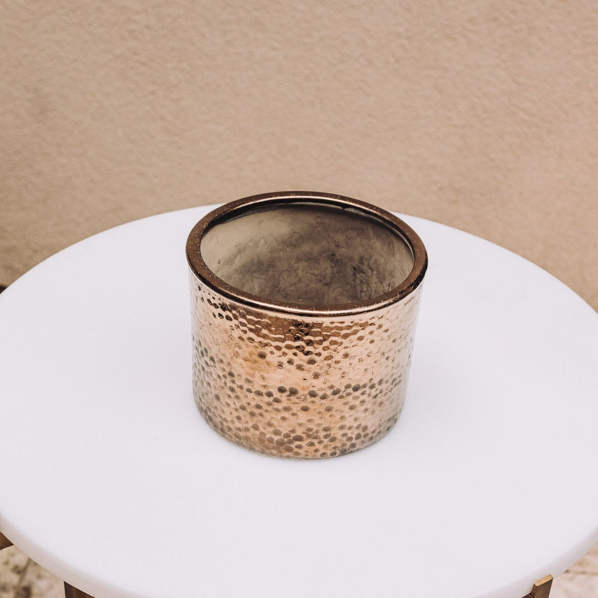 Bronze cylinder pot with textured dimpled glaze and dark rim, displayed on white table